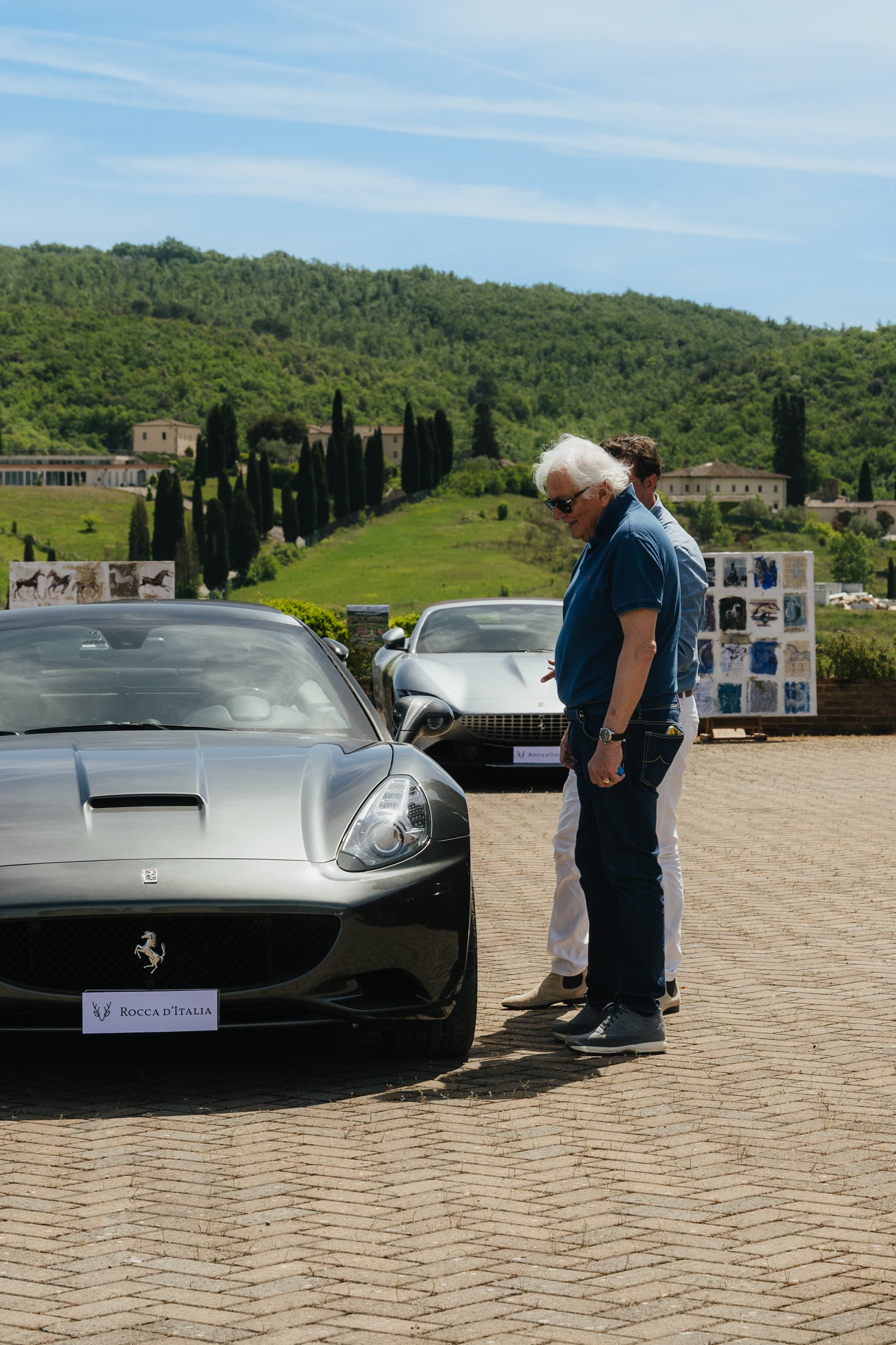 Ferrari grigia con targa Rocca d'Italia e opere d'arte alle colline del Chianti